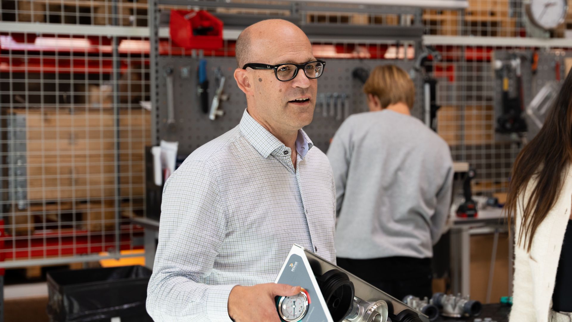 Martin Valfridsson stands in a workshop talking to someone outside of the picture. In the background someone is working with their back towards the camera. 