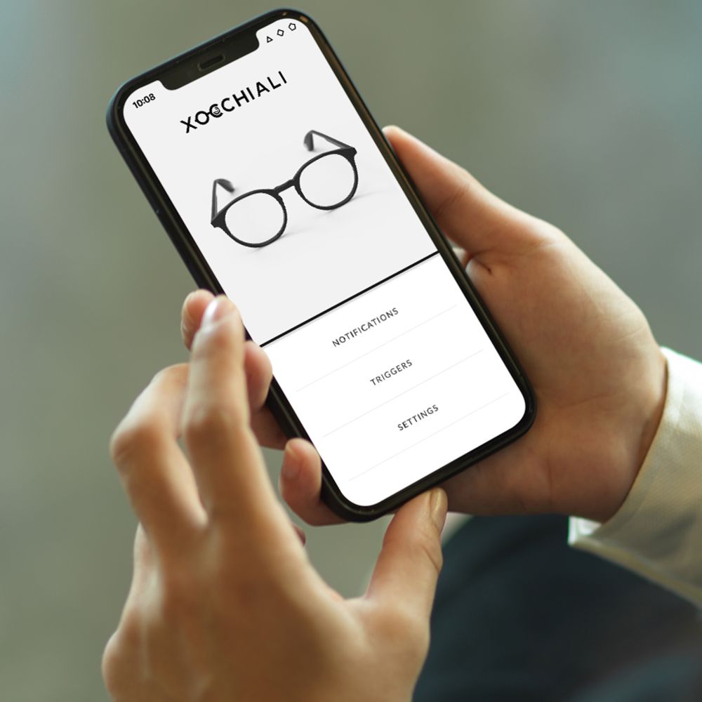 Två händer håller i en smartphone som visar upp Xocchialis app för smarta glasögon.